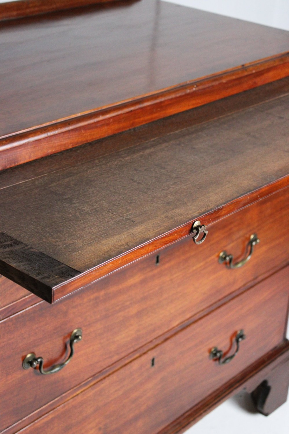 A George III mahogany chest of drawers featuring three graduated long drawers with brass swan-neck handles and bracket feet. View III