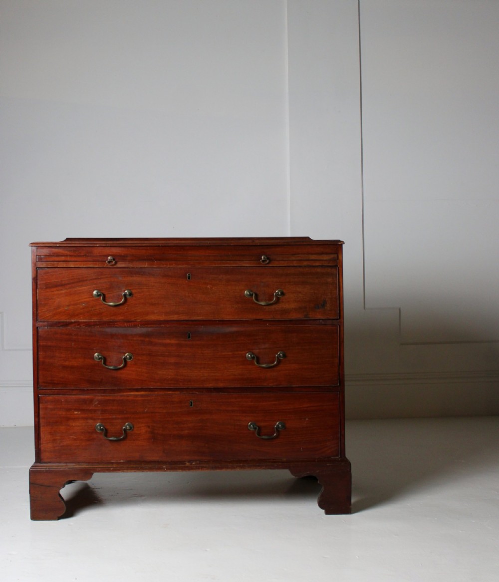 A George III mahogany chest of drawers featuring three graduated long drawers with brass swan-neck handles and bracket feet. View V