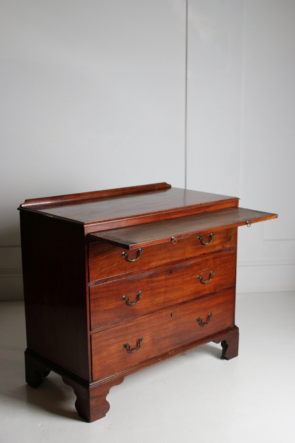 A George III mahogany chest of drawers featuring three graduated long drawers with brass swan-neck handles and bracket feet. View VI