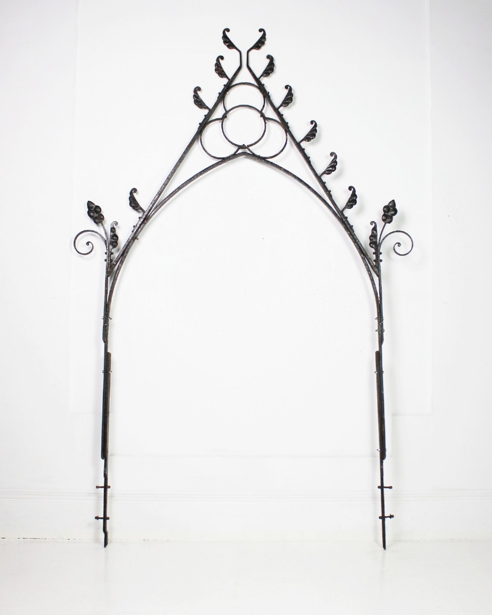 A tall Victorian Gothic Revival iron arch with a pointed apex, decorative crockets along the outer edges, and circular tracery within the upper pediment.
