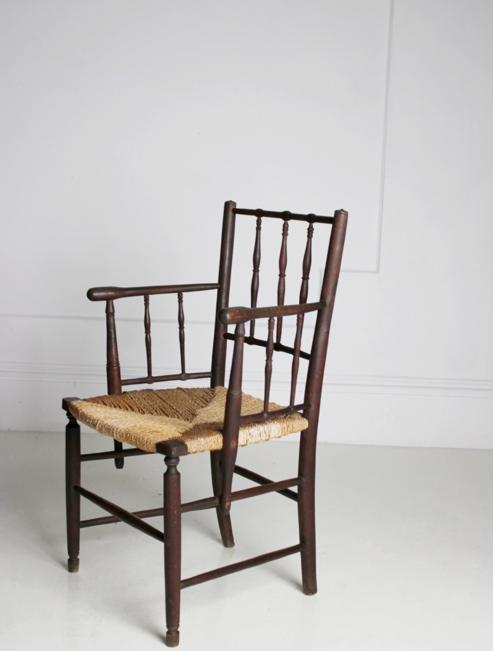 An antique dark-stained beech armchair featuring turned spindle backrests and arm supports with a natural woven rush seat.