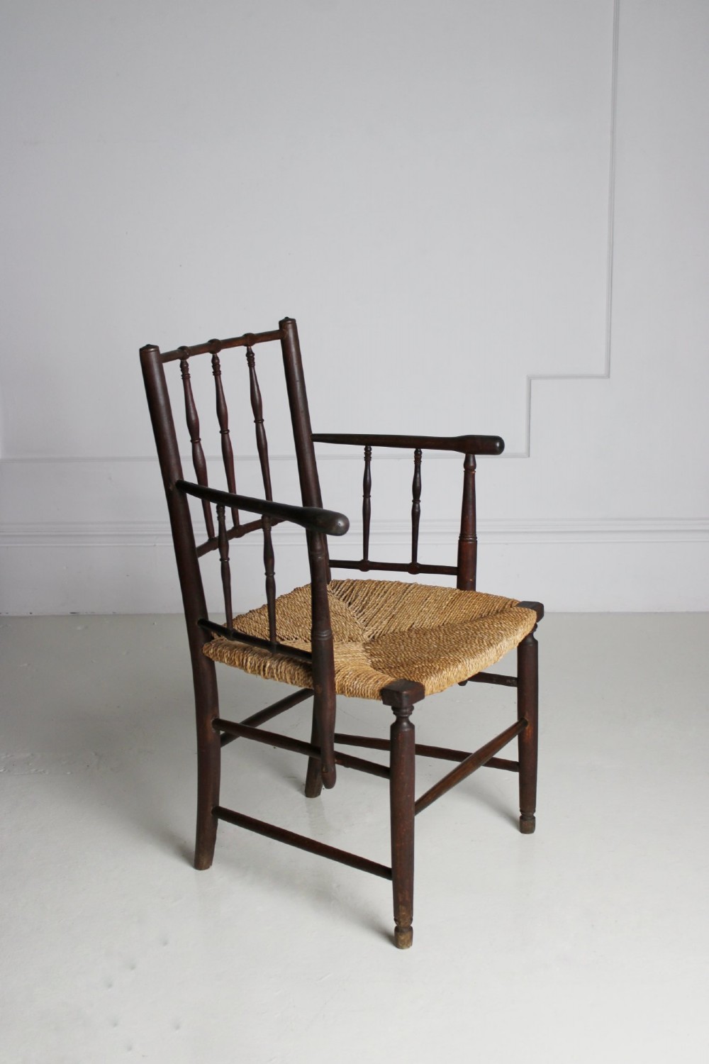 An antique dark-stained beech armchair featuring turned spindle backrests and arm supports with a natural woven rush seat. View II
