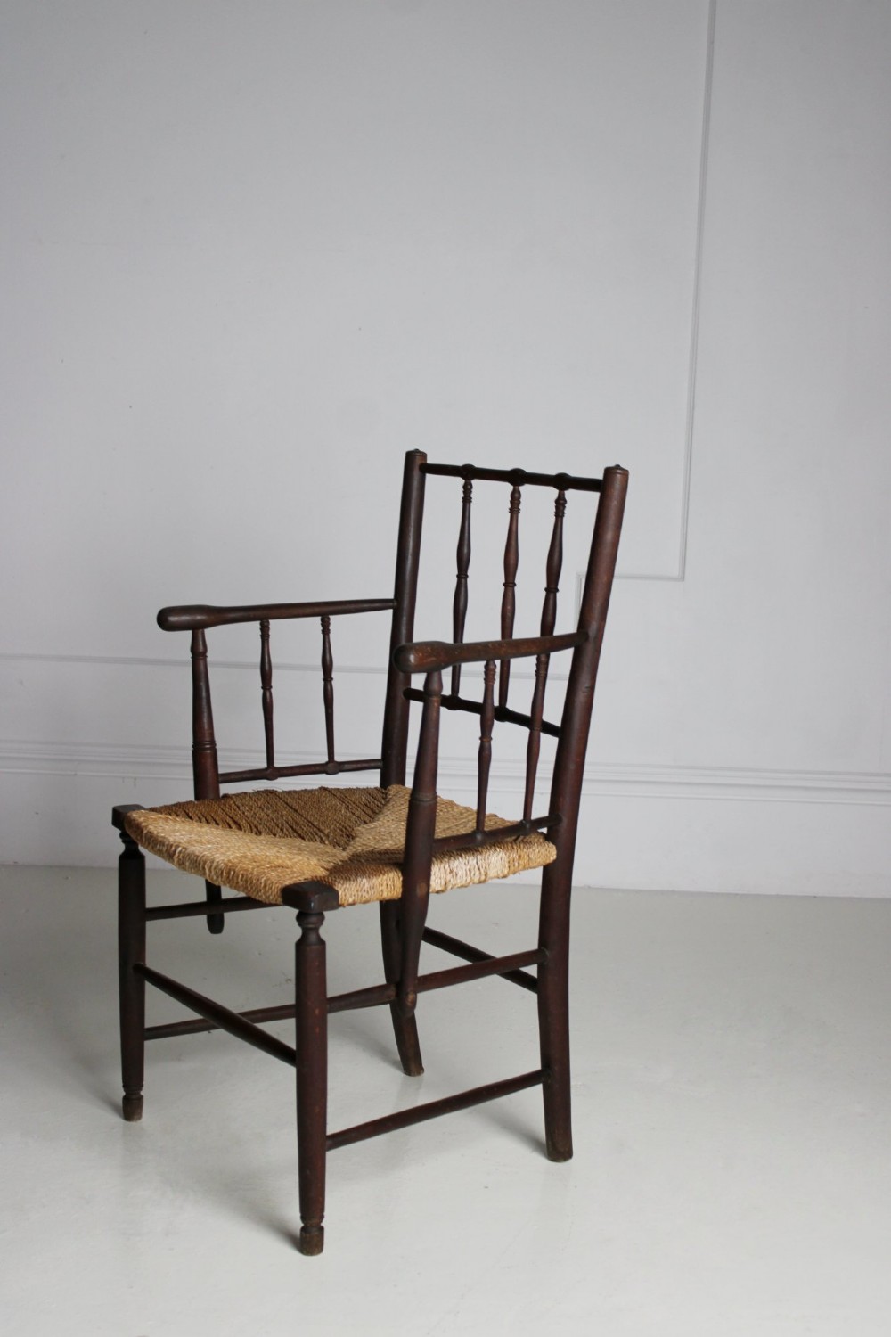 An antique dark-stained beech armchair featuring turned spindle backrests and arm supports with a natural woven rush seat. View III