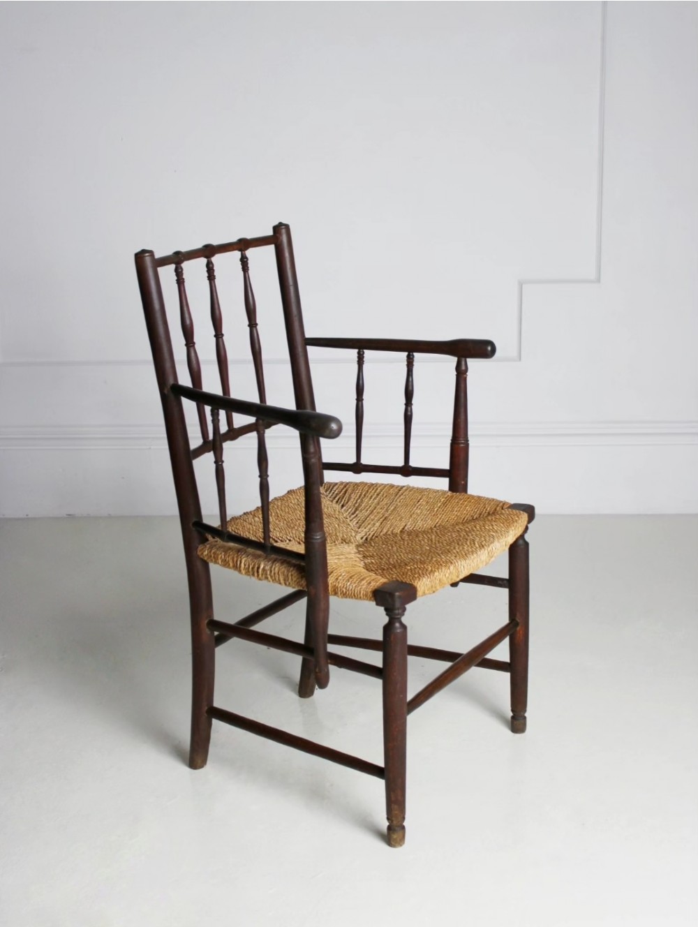 An antique dark-stained beech armchair featuring turned spindle backrests and arm supports with a natural woven rush seat. View IV