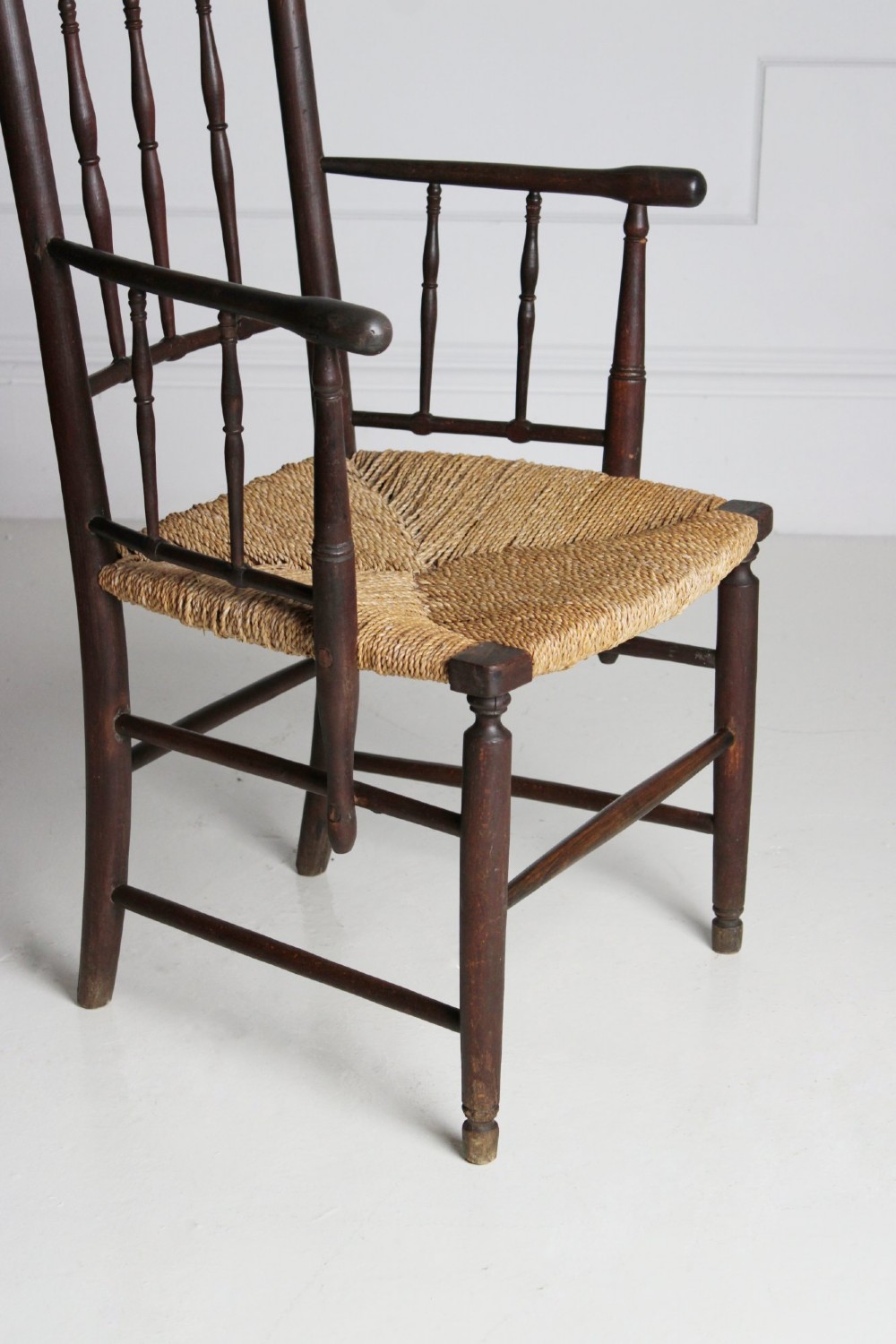 An antique dark-stained beech armchair featuring turned spindle backrests and arm supports with a natural woven rush seat. View V