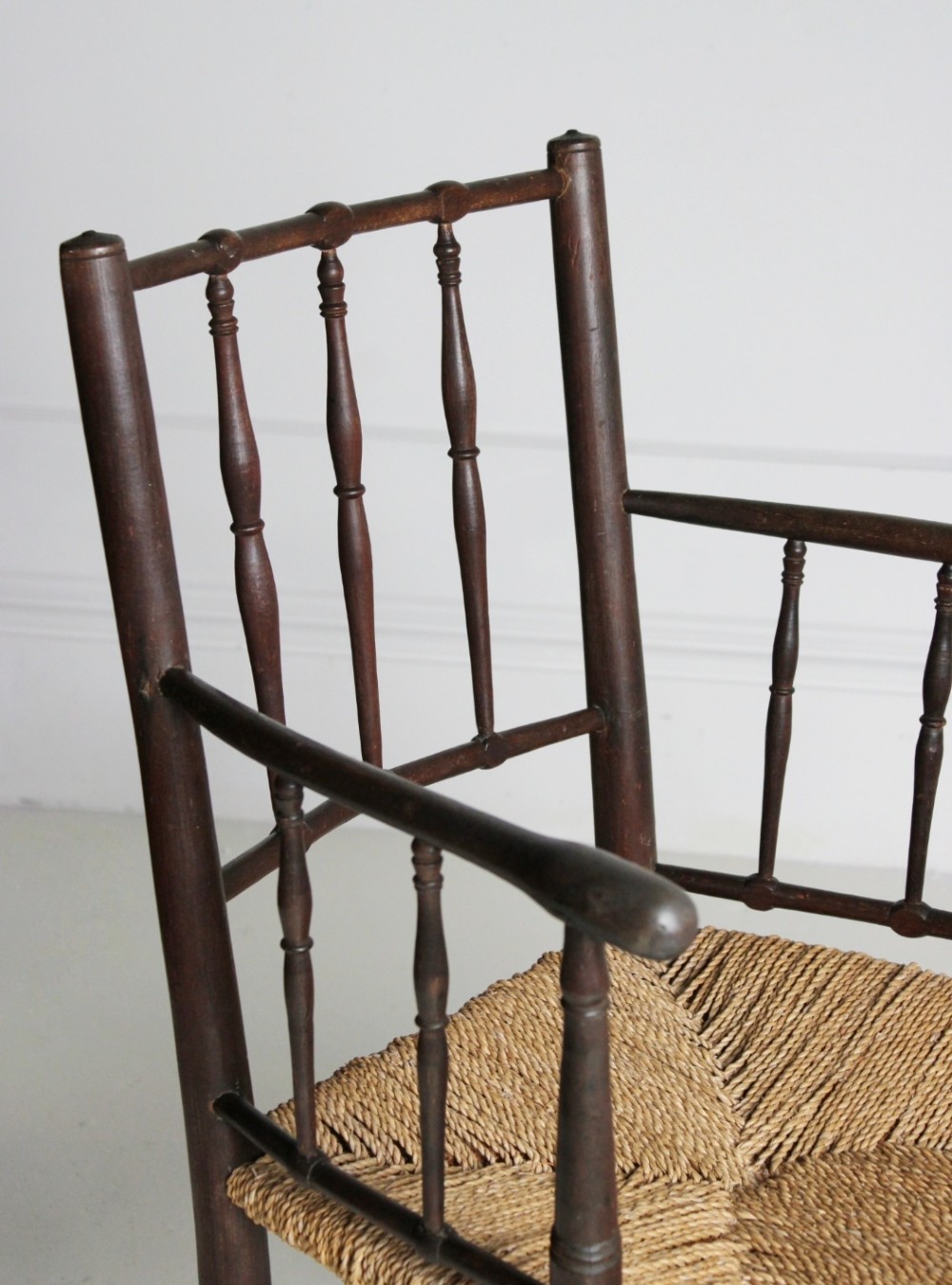 An antique dark-stained beech armchair featuring turned spindle backrests and arm supports with a natural woven rush seat. View VII