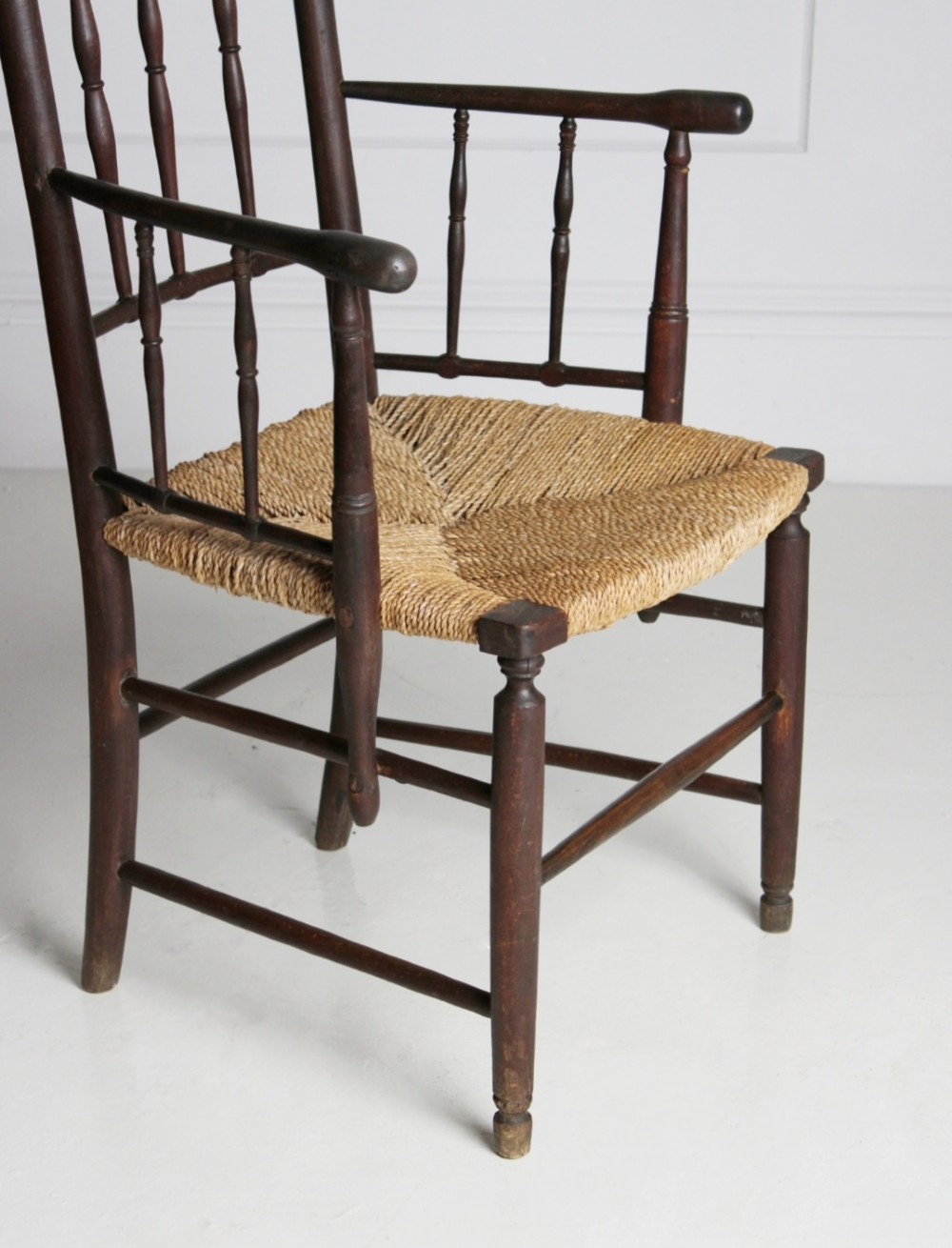 An antique dark-stained beech armchair featuring turned spindle backrests and arm supports with a natural woven rush seat. View IX