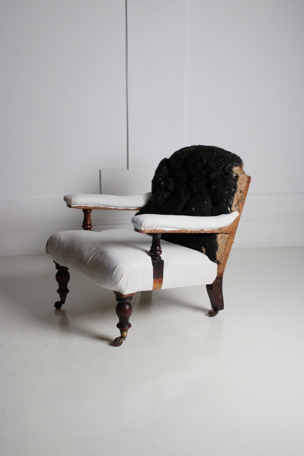 A 19th-century Victorian armchair lined in off-white calico with turned mahogany legs, brass castors, and a buttoned horsehair backrest.