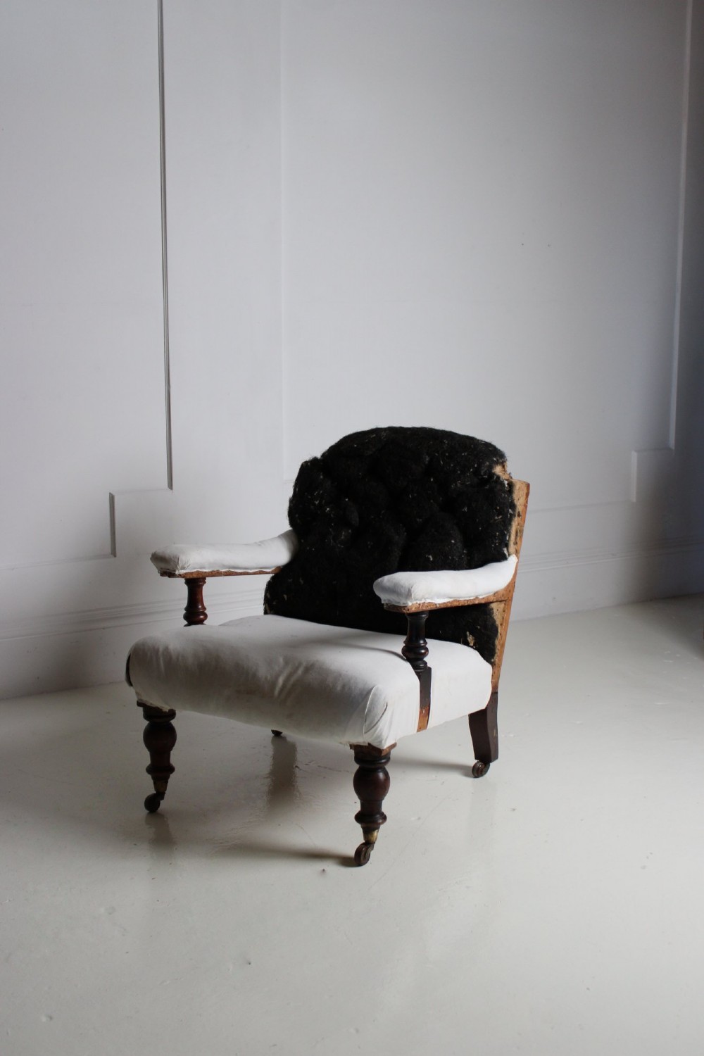 A 19th-century Victorian armchair lined in off-white calico with turned mahogany legs, brass castors, and a buttoned horsehair backrest. View IV