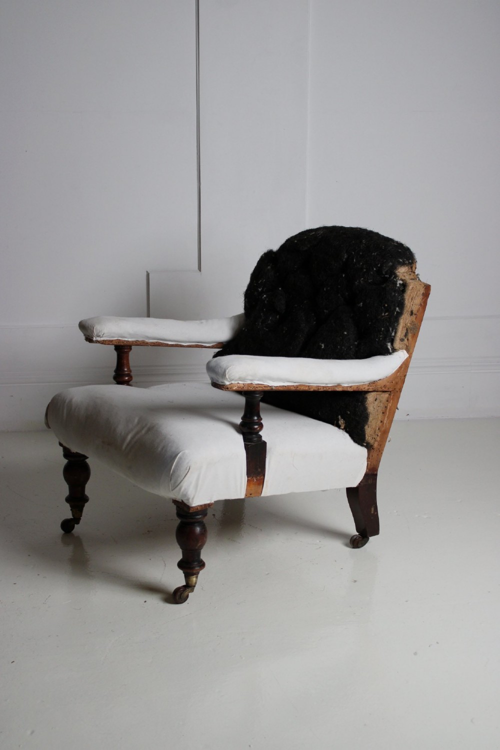 A 19th-century Victorian armchair lined in off-white calico with turned mahogany legs, brass castors, and a buttoned horsehair backrest. View V