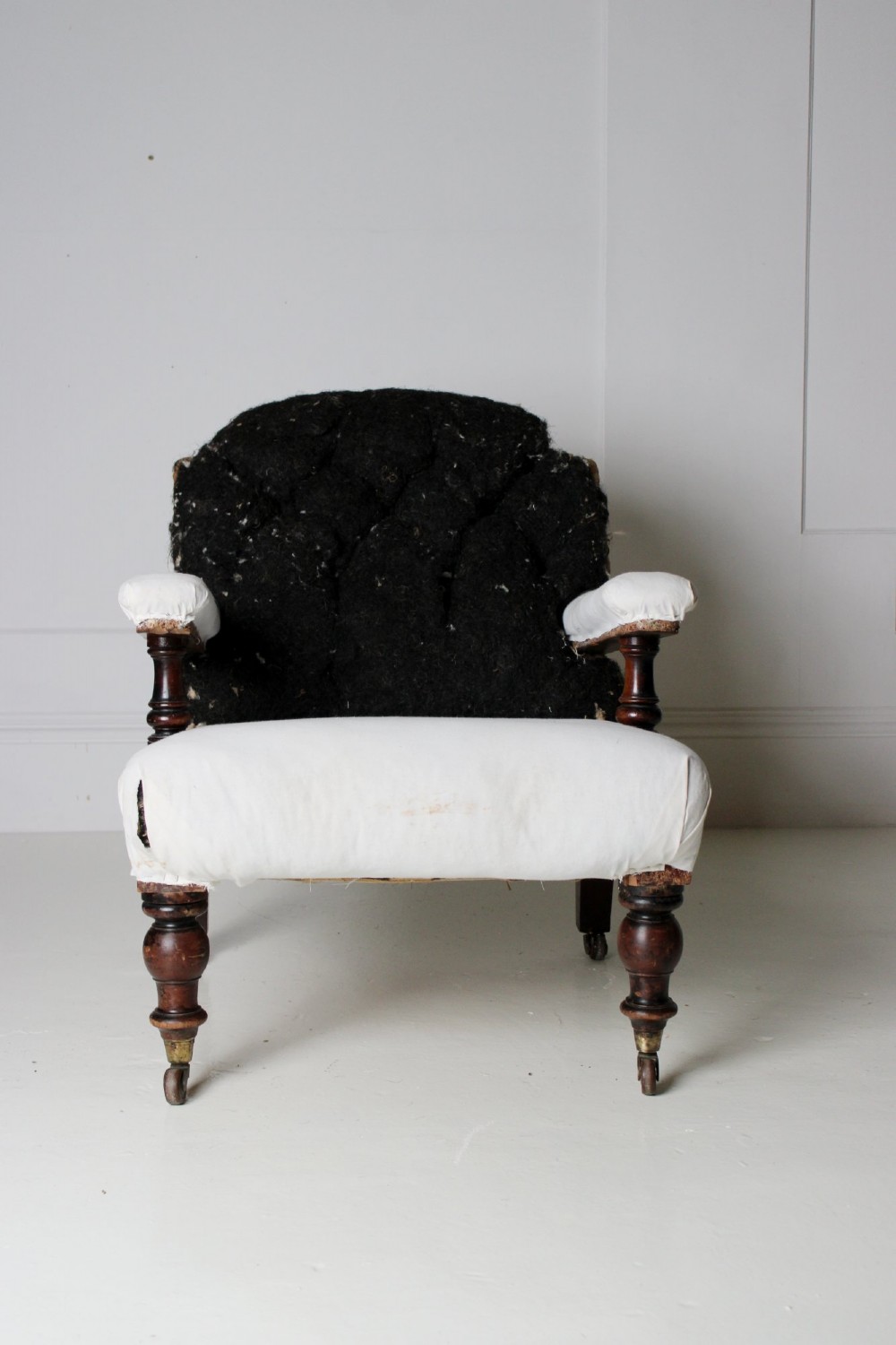 A 19th-century Victorian armchair lined in off-white calico with turned mahogany legs, brass castors, and a buttoned horsehair backrest. View IX