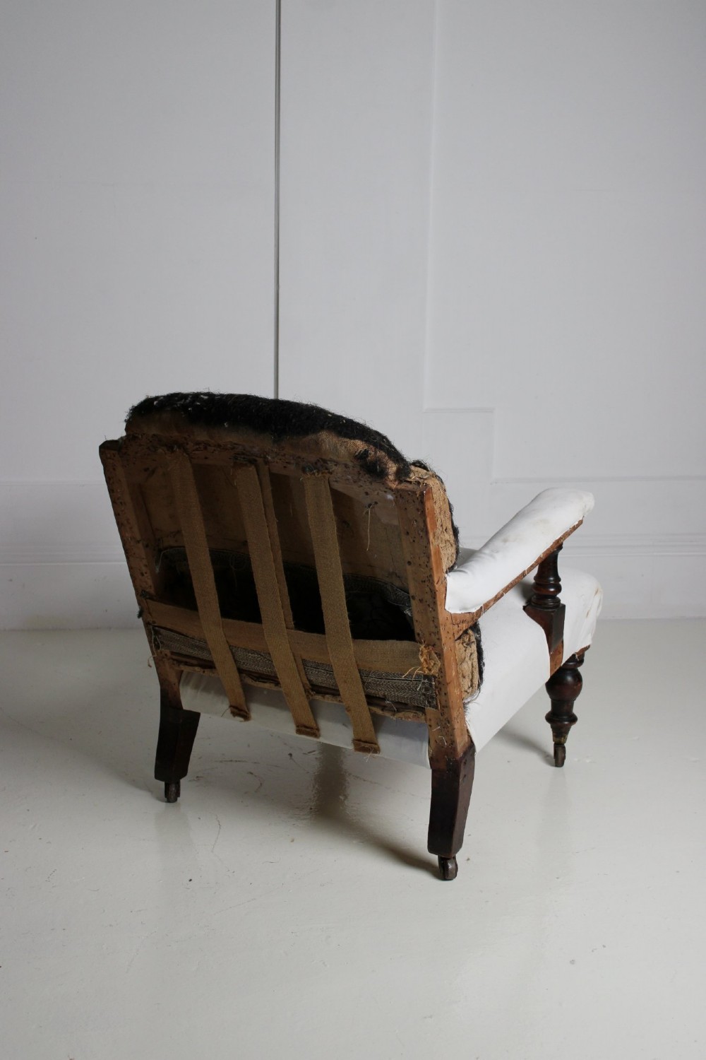 A 19th-century Victorian armchair lined in off-white calico with turned mahogany legs, brass castors, and a buttoned horsehair backrest. View X