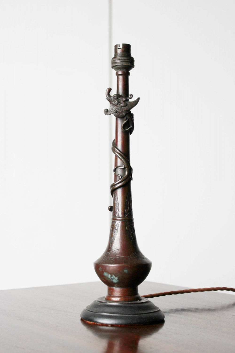 An antique dark bronze table lamp base featuring a sculpted dragon wrapped around a slender stem above a rounded base.
