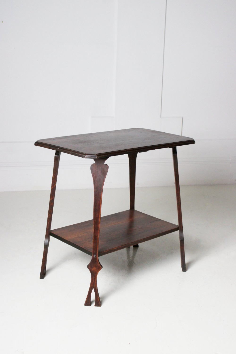 An Arts and Crafts dark oak side table featuring a rectangular top, a lower tier shelf, and stylized tapered legs with spade cutouts.
