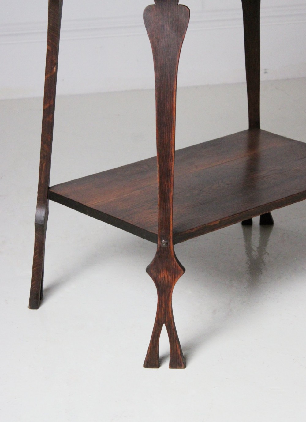 An Arts and Crafts dark oak side table featuring a rectangular top, a lower tier shelf, and stylized tapered legs with spade cutouts. View II