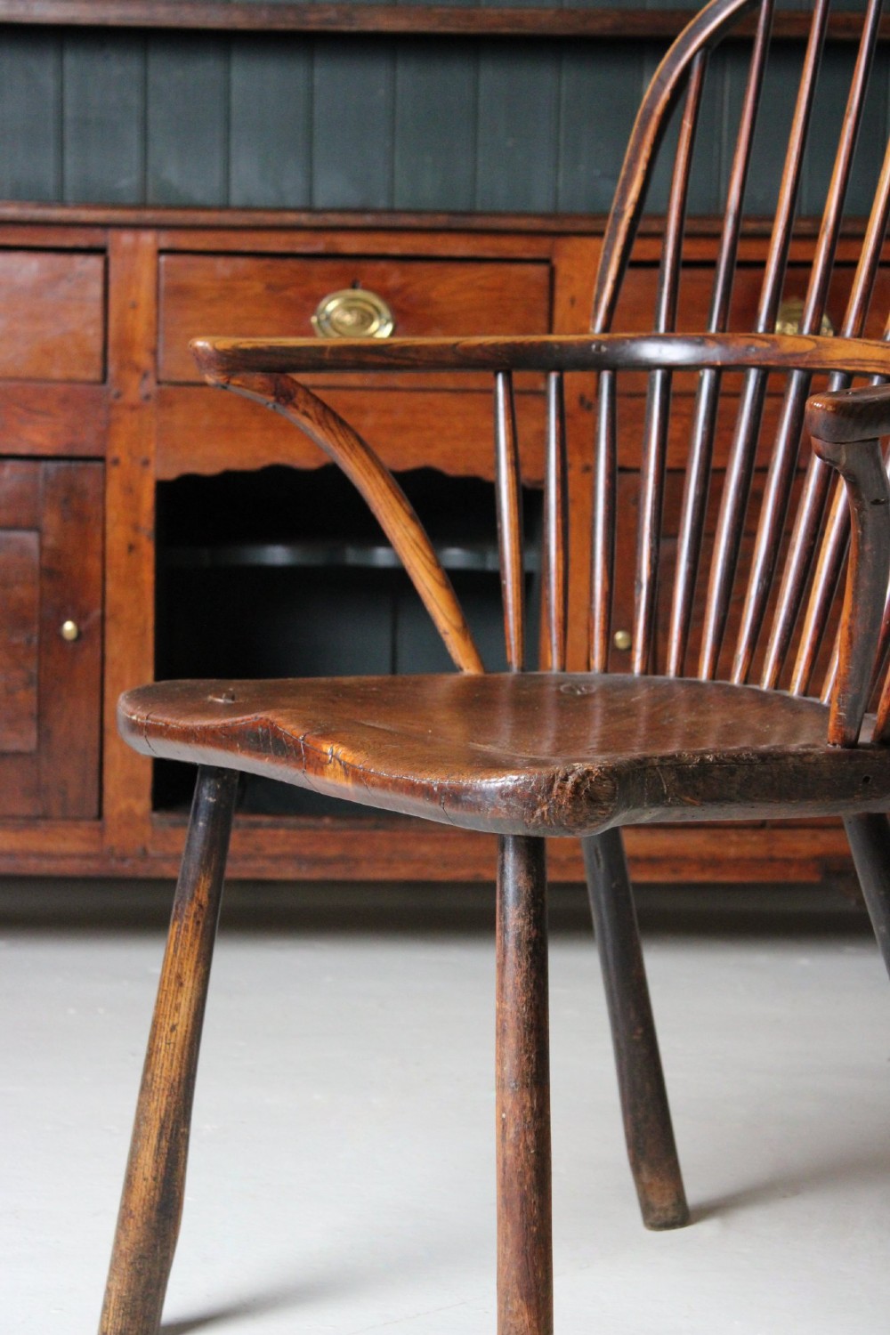 An 18th-century vernacular wooden Windsor armchair featuring a steam-bent hoop back, slender spindles, a carved saddle seat, and splayed legs. View II