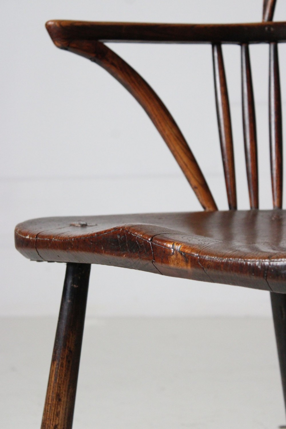 An 18th-century vernacular wooden Windsor armchair featuring a steam-bent hoop back, slender spindles, a carved saddle seat, and splayed legs. View III