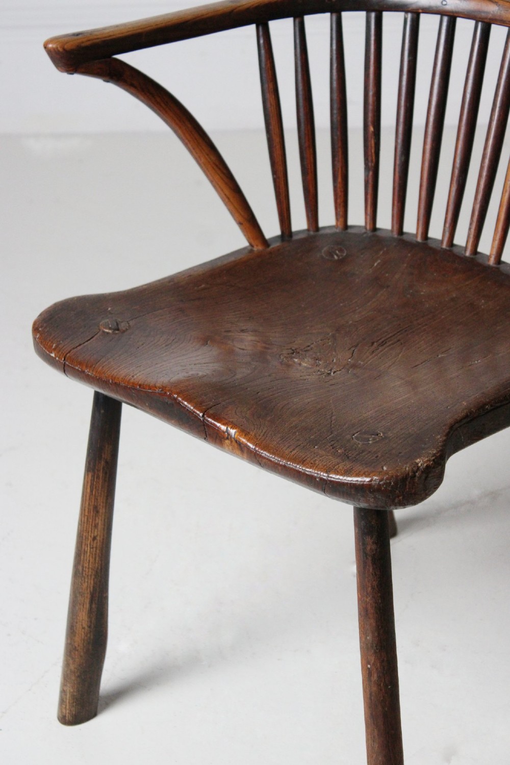 An 18th-century vernacular wooden Windsor armchair featuring a steam-bent hoop back, slender spindles, a carved saddle seat, and splayed legs. View IV