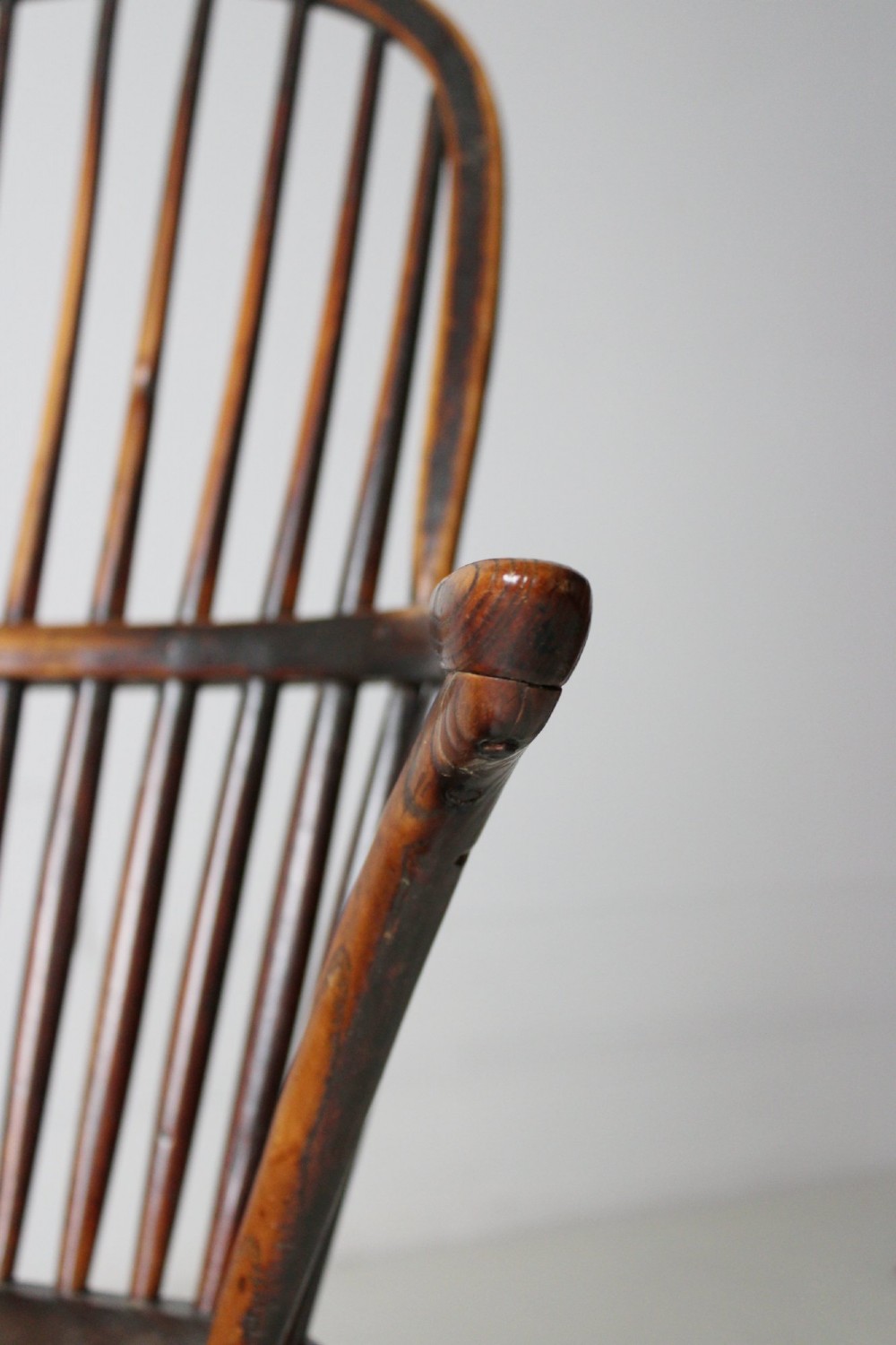 An 18th-century vernacular wooden Windsor armchair featuring a steam-bent hoop back, slender spindles, a carved saddle seat, and splayed legs. View V
