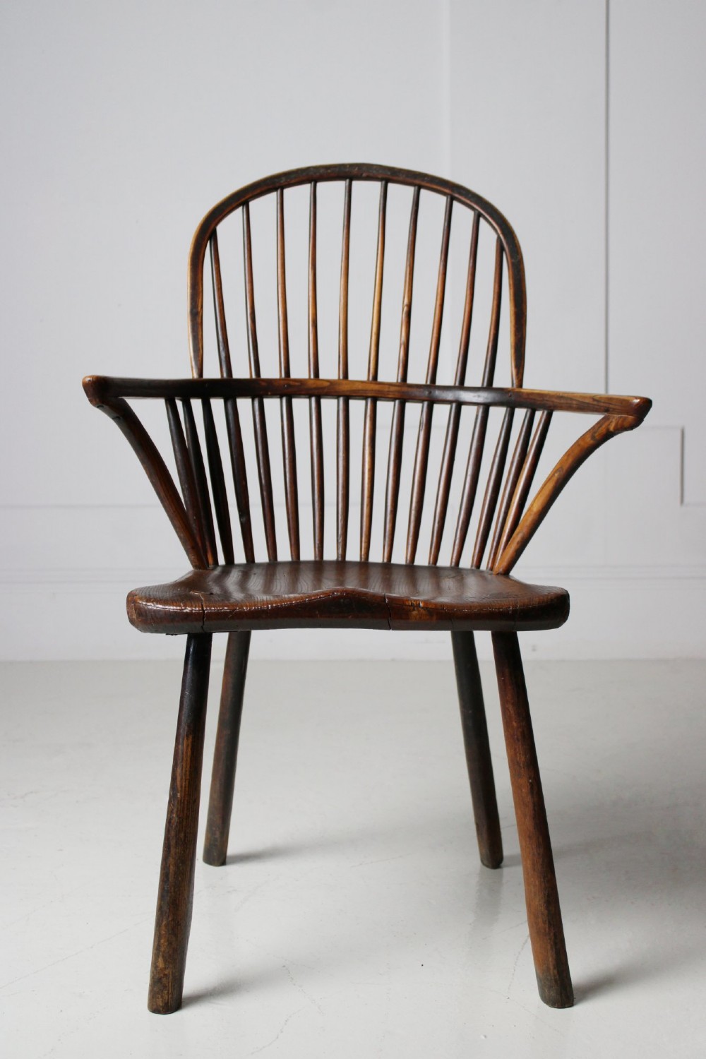 An 18th-century vernacular wooden Windsor armchair featuring a steam-bent hoop back, slender spindles, a carved saddle seat, and splayed legs. View VI
