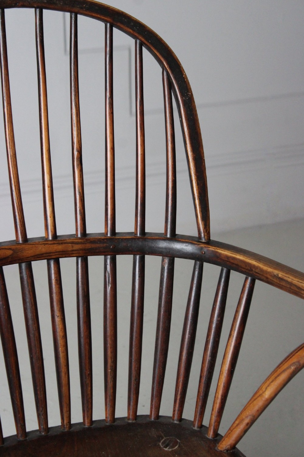 An 18th-century vernacular wooden Windsor armchair featuring a steam-bent hoop back, slender spindles, a carved saddle seat, and splayed legs. View VII