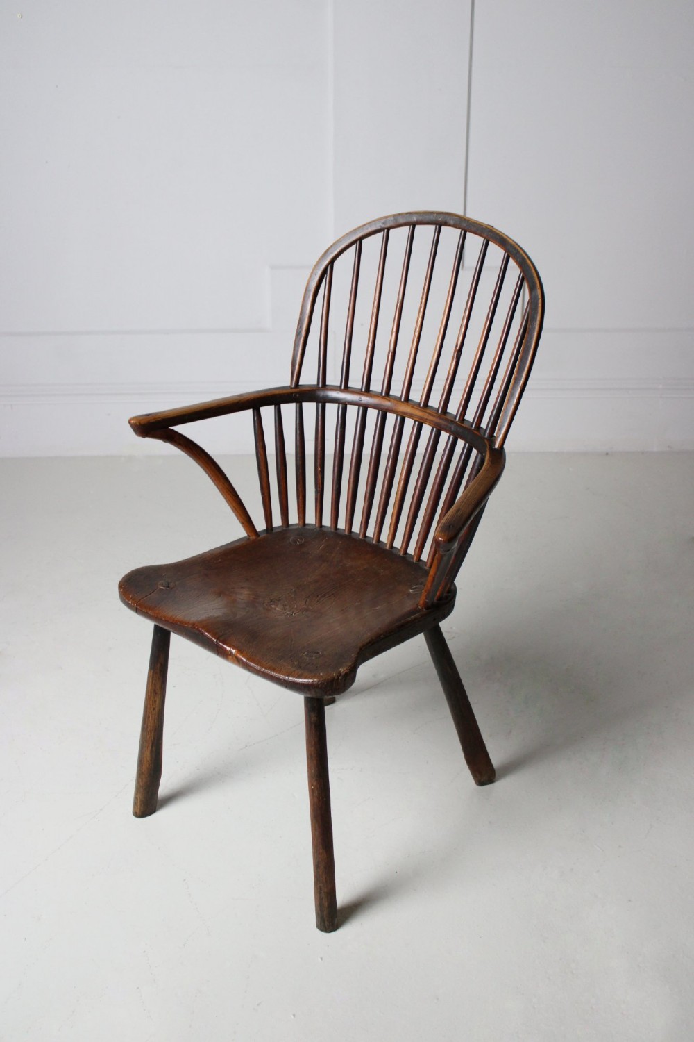 An 18th-century vernacular wooden Windsor armchair featuring a steam-bent hoop back, slender spindles, a carved saddle seat, and splayed legs. View VIII