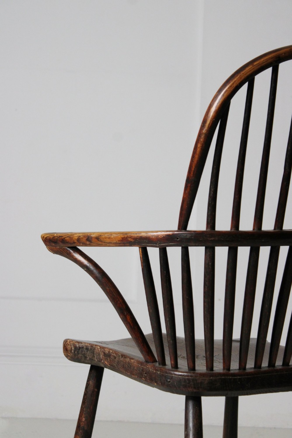 An 18th-century vernacular wooden Windsor armchair featuring a steam-bent hoop back, slender spindles, a carved saddle seat, and splayed legs. View IX