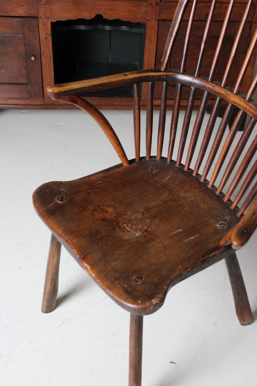 An 18th-century vernacular wooden Windsor armchair featuring a steam-bent hoop back, slender spindles, a carved saddle seat, and splayed legs. View X