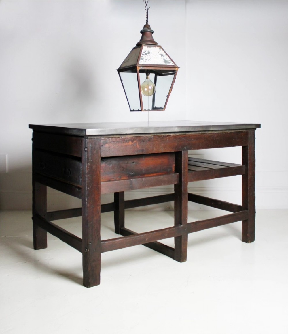 A heavy Victorian dark wood industrial typesetting table featuring a flat metal surface, deep storage drawers, and robust square legs.