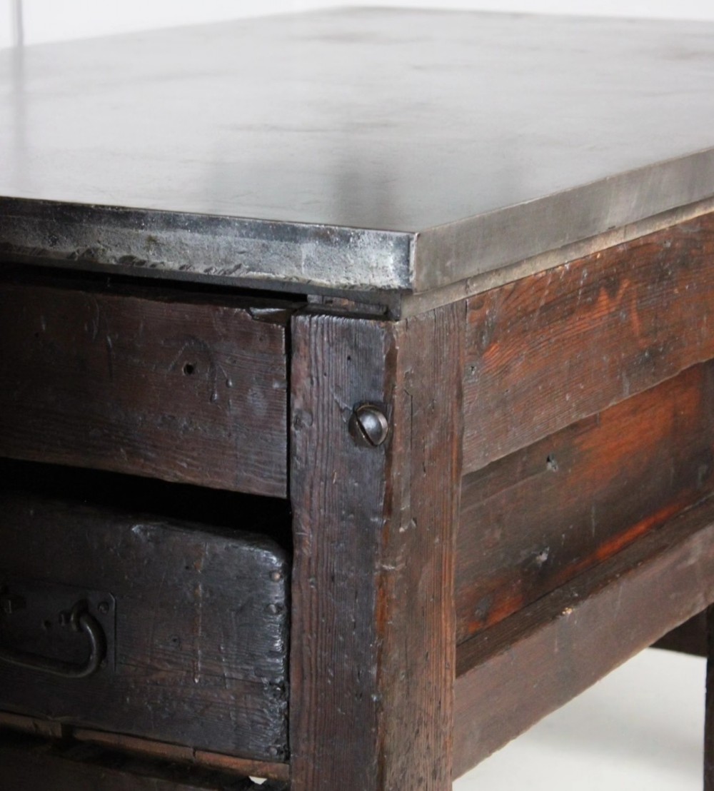 A heavy Victorian dark wood industrial typesetting table featuring a flat metal surface, deep storage drawers, and robust square legs. View IV