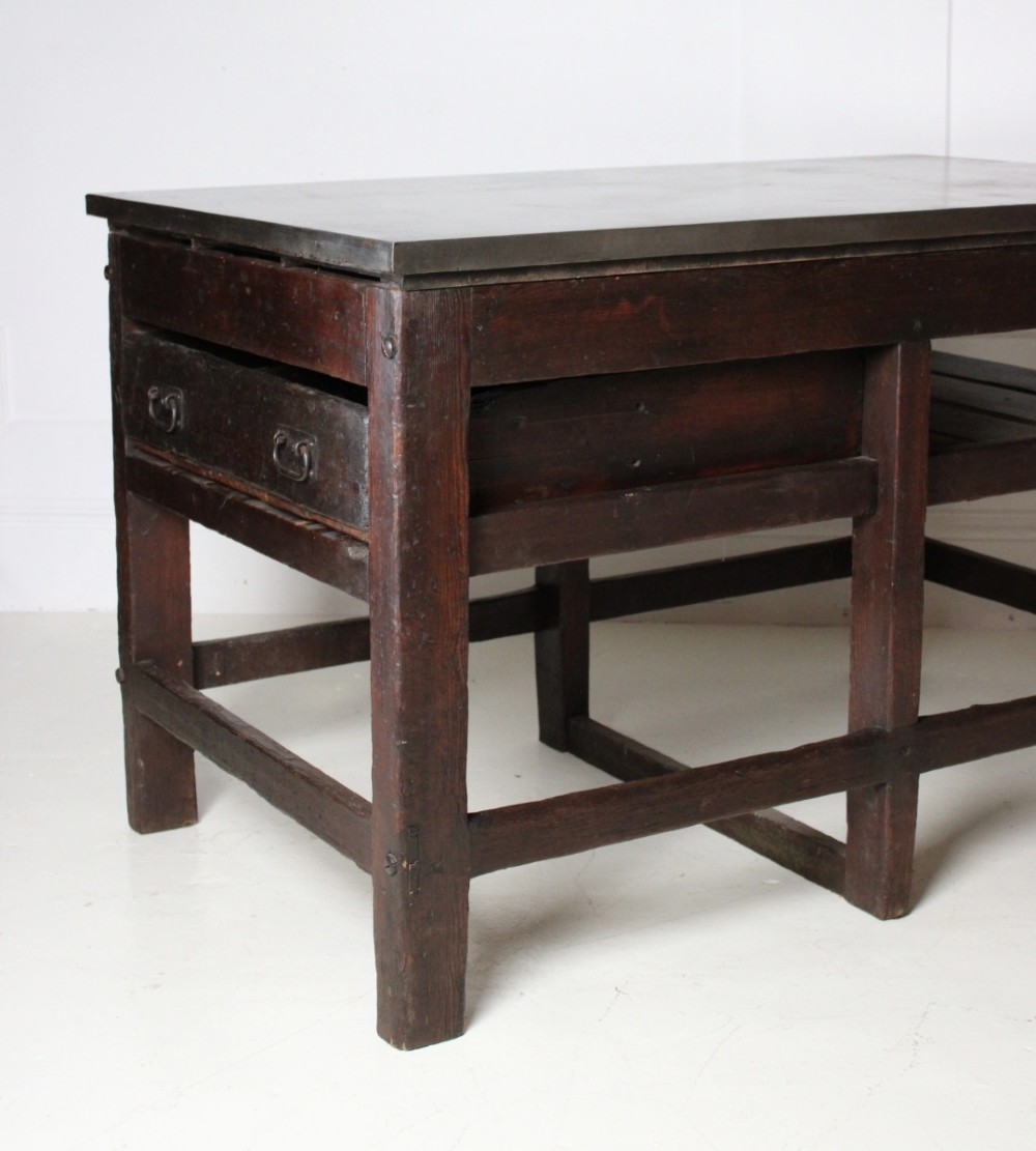 A heavy Victorian dark wood industrial typesetting table featuring a flat metal surface, deep storage drawers, and robust square legs. View V