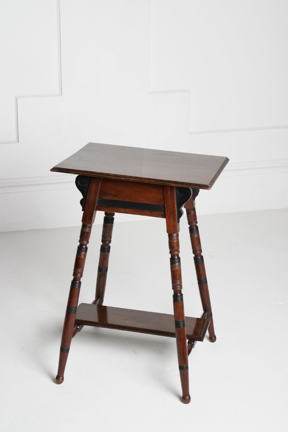 A tall rectangular dark mahogany lamp table featuring turned legs with ebonised bands, a lower undertier, and shaped corner brackets. View III