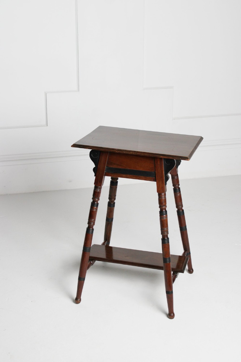 A tall rectangular dark mahogany lamp table featuring turned legs with ebonised bands, a lower undertier, and shaped corner brackets. View IV