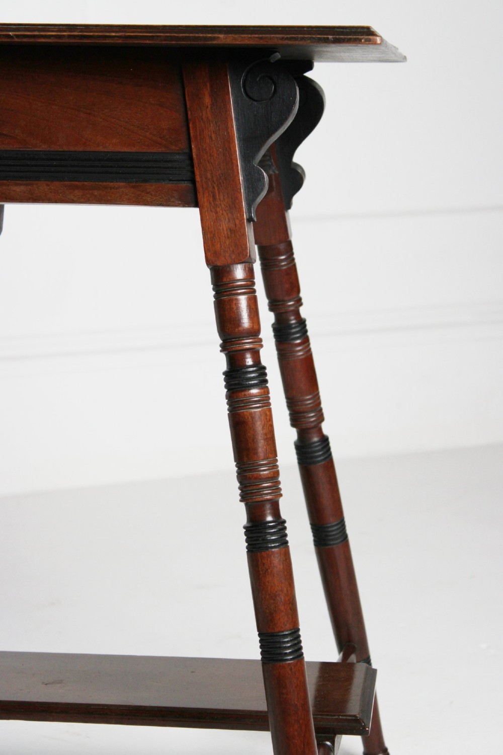 A tall rectangular dark mahogany lamp table featuring turned legs with ebonised bands, a lower undertier, and shaped corner brackets. View VI