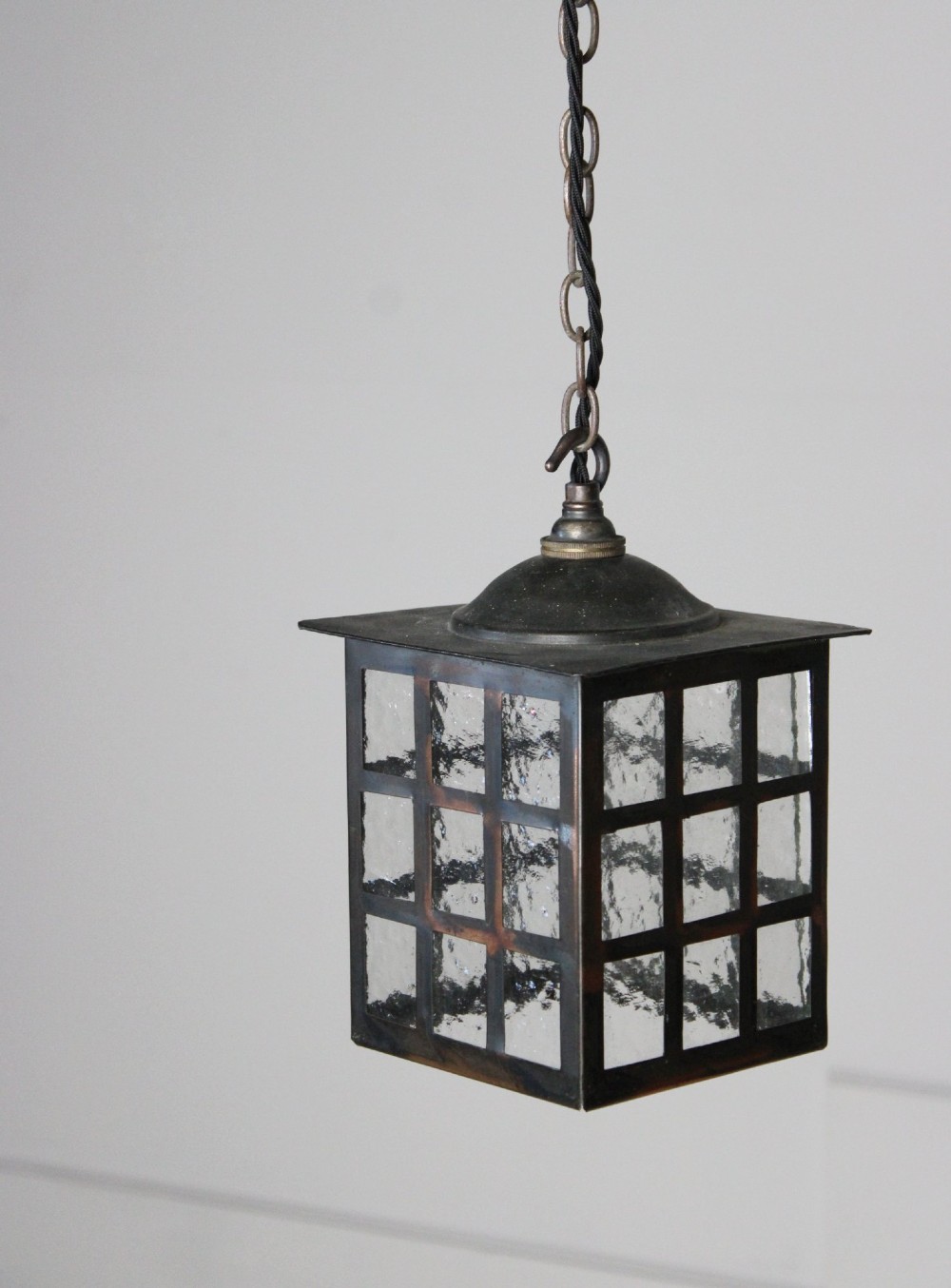 A square dark copper lantern featuring grid-pattern glazed sides with textured glass, hanging from a metal chain.