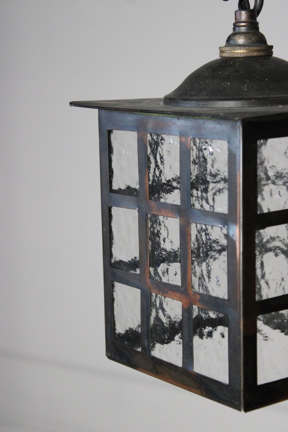 A square dark copper lantern featuring grid-pattern glazed sides with textured glass, hanging from a metal chain. View III