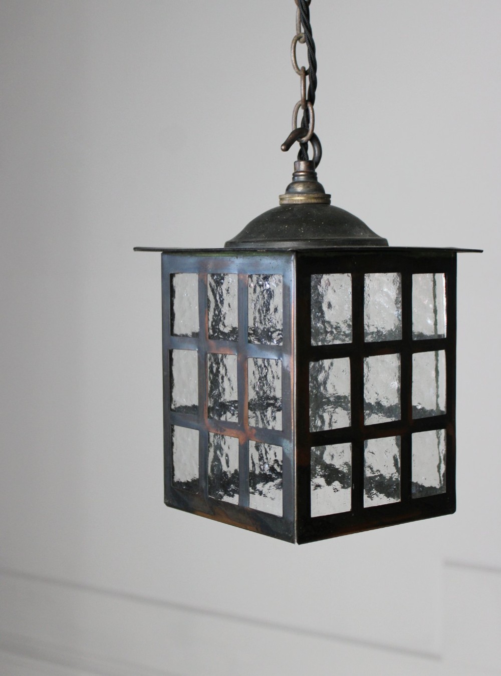 A square dark copper lantern featuring grid-pattern glazed sides with textured glass, hanging from a metal chain. View IV