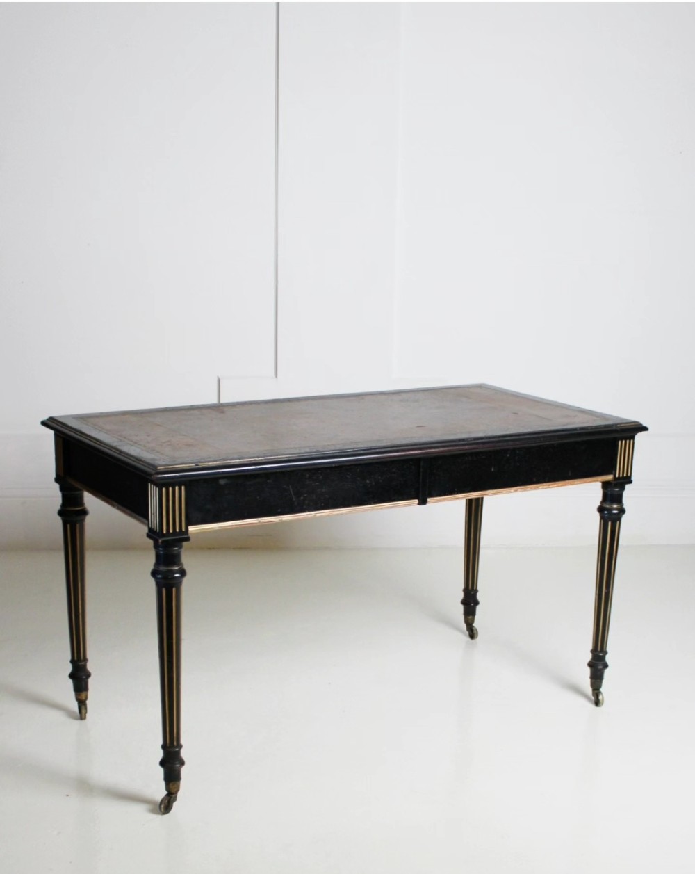 An ebonised Aesthetic Movement library writing table featuring gilt fluted legs, brass castors, and a leather inset top.