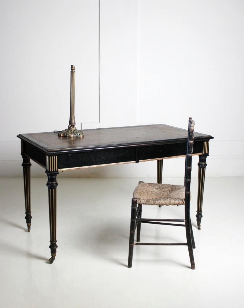 An ebonised Aesthetic Movement library writing table featuring gilt fluted legs, brass castors, and a leather inset top. View II