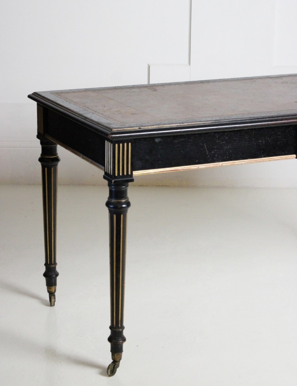 An ebonised Aesthetic Movement library writing table featuring gilt fluted legs, brass castors, and a leather inset top. View III
