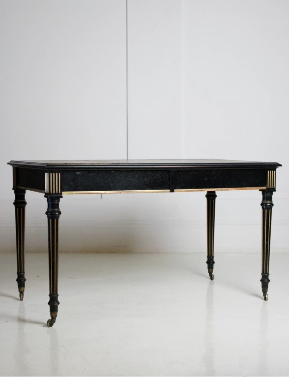 An ebonised Aesthetic Movement library writing table featuring gilt fluted legs, brass castors, and a leather inset top. View IV