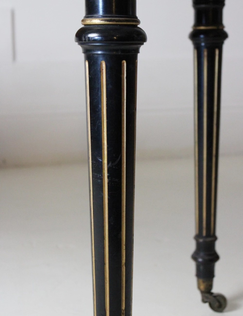 An ebonised Aesthetic Movement library writing table featuring gilt fluted legs, brass castors, and a leather inset top. View V