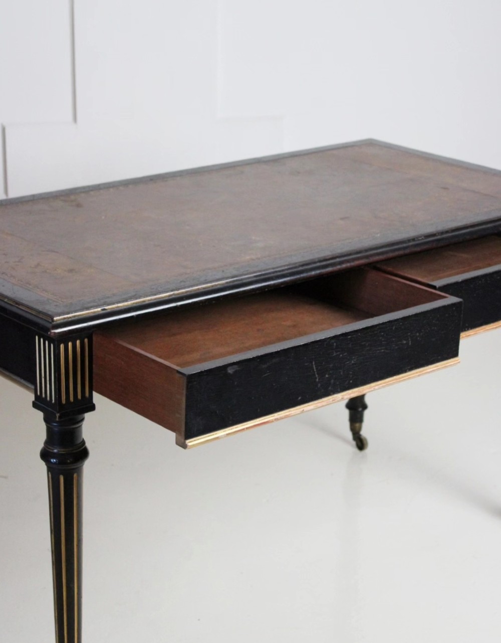 An ebonised Aesthetic Movement library writing table featuring gilt fluted legs, brass castors, and a leather inset top. View VI