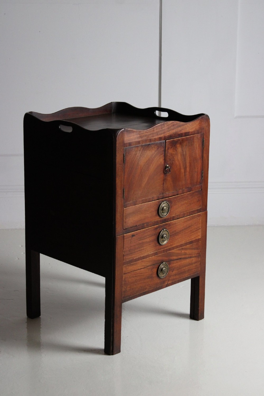 A George III mahogany pot cupboard with a shaped tray top, a two-door cabinet section, and three drawers fitted with brass ring handles. View II