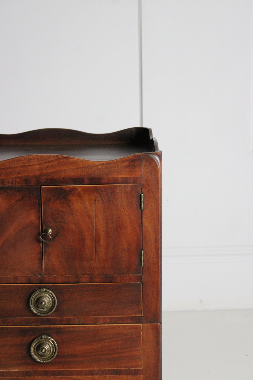 A George III mahogany pot cupboard with a shaped tray top, a two-door cabinet section, and three drawers fitted with brass ring handles. View V