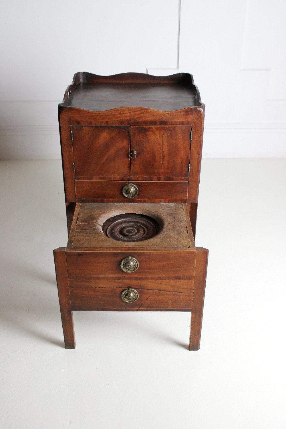A George III mahogany pot cupboard with a shaped tray top, a two-door cabinet section, and three drawers fitted with brass ring handles. View VI