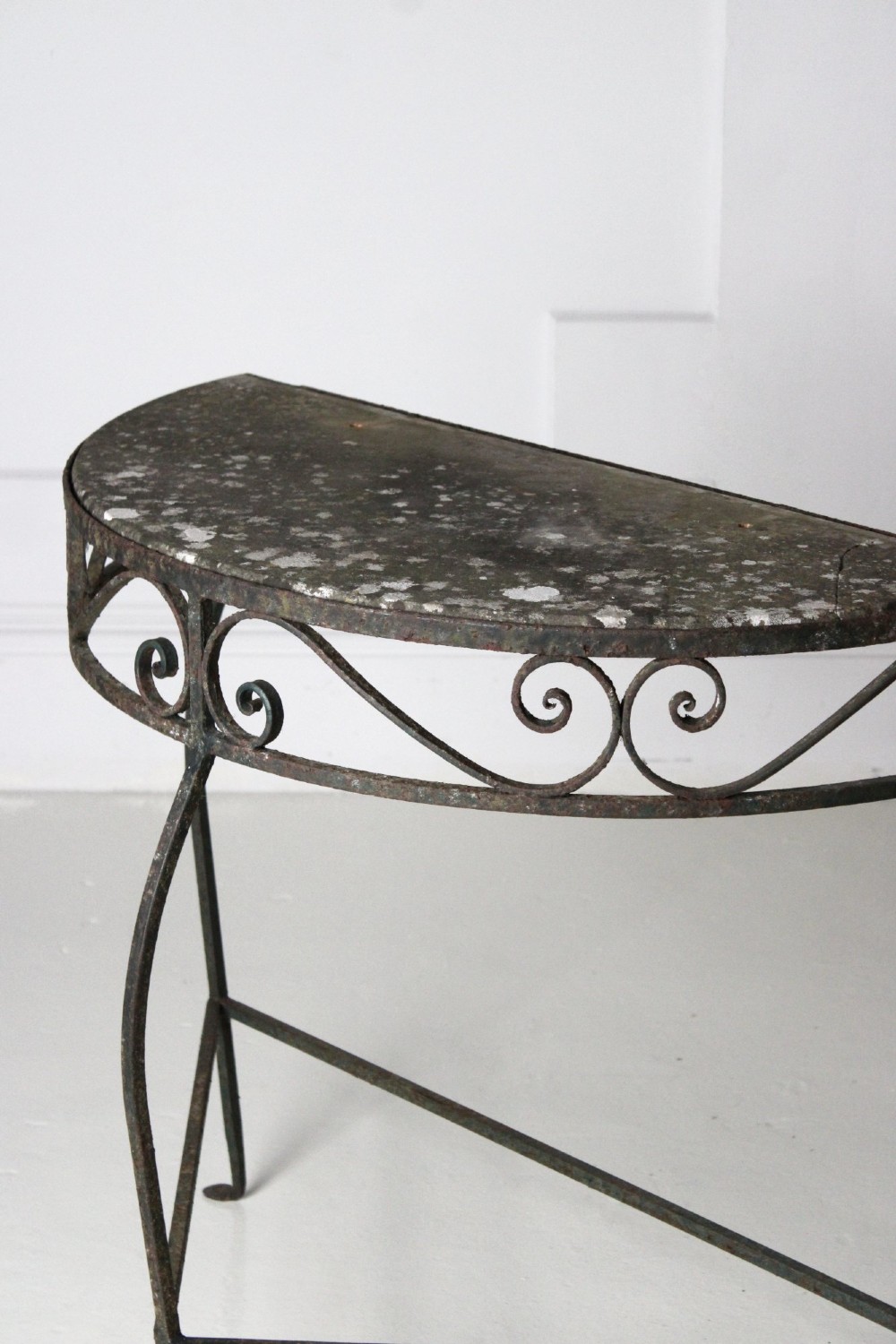 A demilune wrought iron console table featuring scrollwork decoration along the apron and a weathered dark marble top. View VI