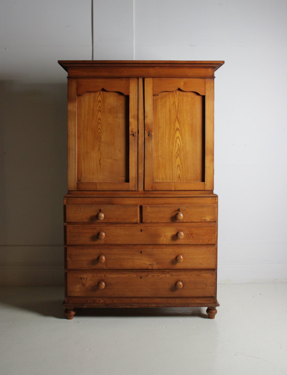 A 19th-century ash linen press featuring double cabinet doors open to reveal green-painted interior shelves over a chest of five drawers with turned wooden handles. View V