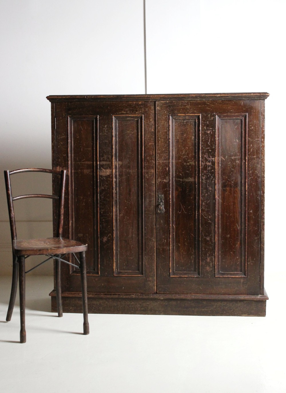 A 19th-century dark stained pine cupboard featuring double-panelled doors, a plinth base, and surface scratches.
