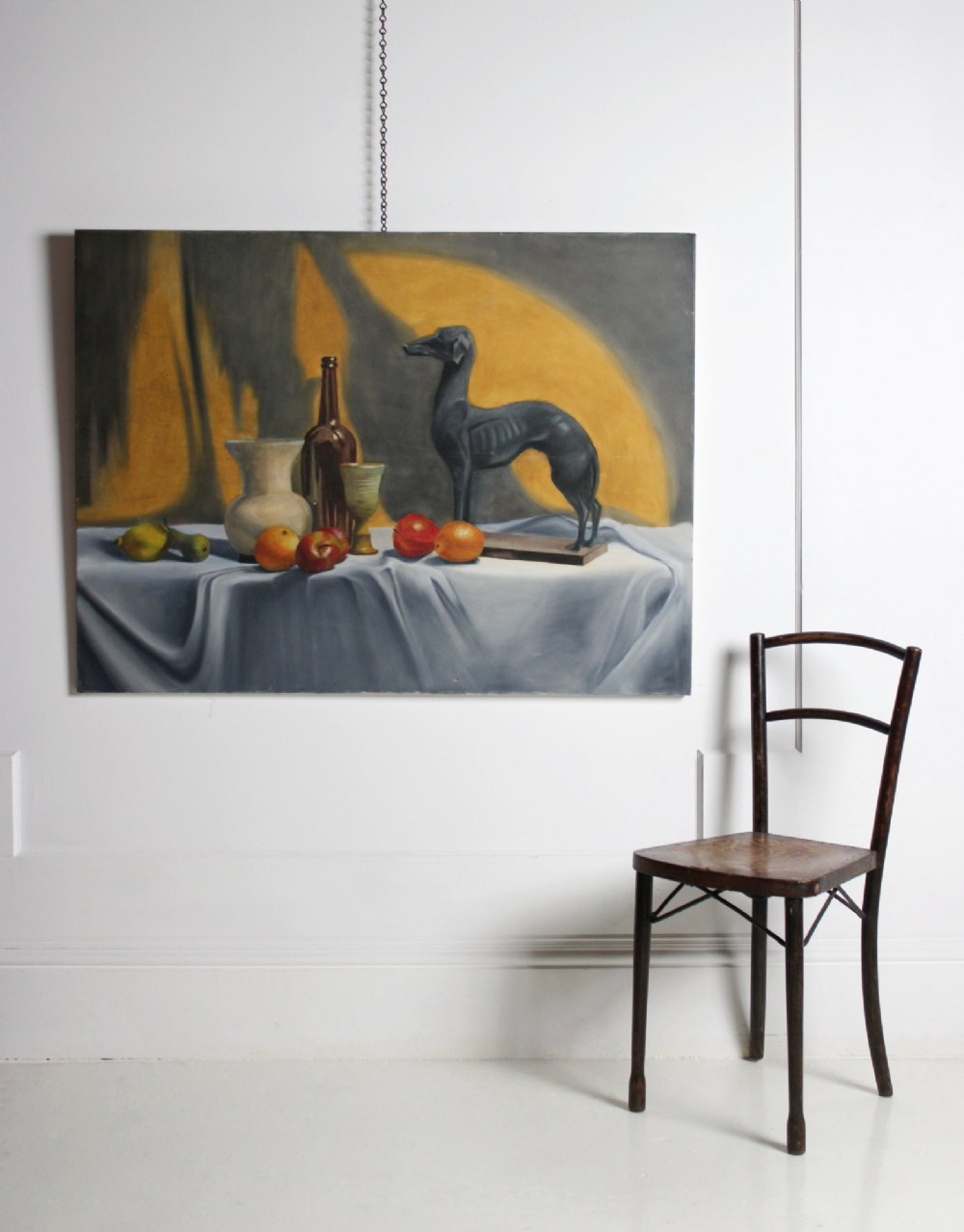 A large mid-20th-century oil painting depicting a draped tabletop still life with fruit, ceramic vessels, and a dark greyhound sculpture against a yellow and grey backdrop.